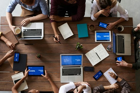 Geschäftsleute sitzen an einem Konferenztisch, arbeiten an Laptops und diskutieren.