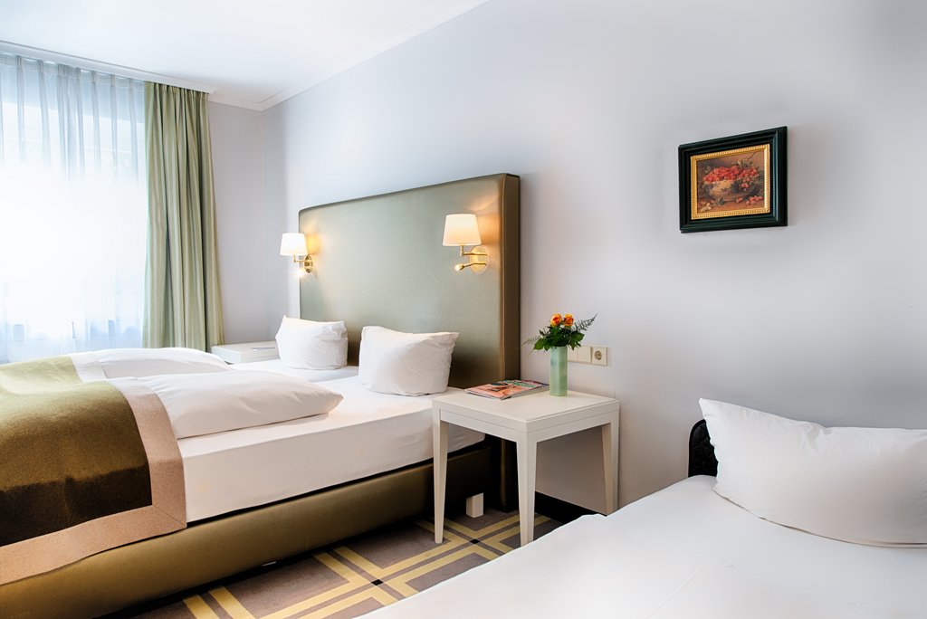 hotelscheiberhof-bett.jpg Modern eingerichtetes Hotelzimmer mit großem Bett und hochwertiger Einrichtung.