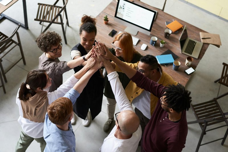 Mehrere Personen in Businesskleidung stehen in einem modernen Büro und geben sich gut gelaunt einen gemeinsamen High-Five.